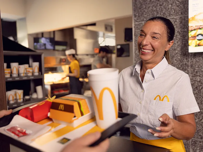McDonald’s Mitarbeiterin überreicht einem Gast seine Bestellung